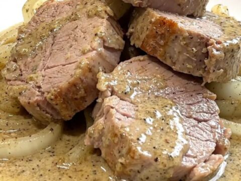 A close-up of tender pork medallions topped with a creamy peppercorn sauce and soft onions in a slow cooker.