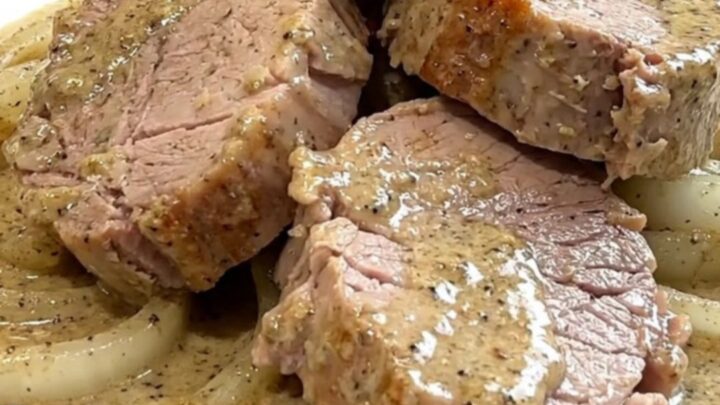A close-up of tender pork medallions topped with a creamy peppercorn sauce and soft onions in a slow cooker.