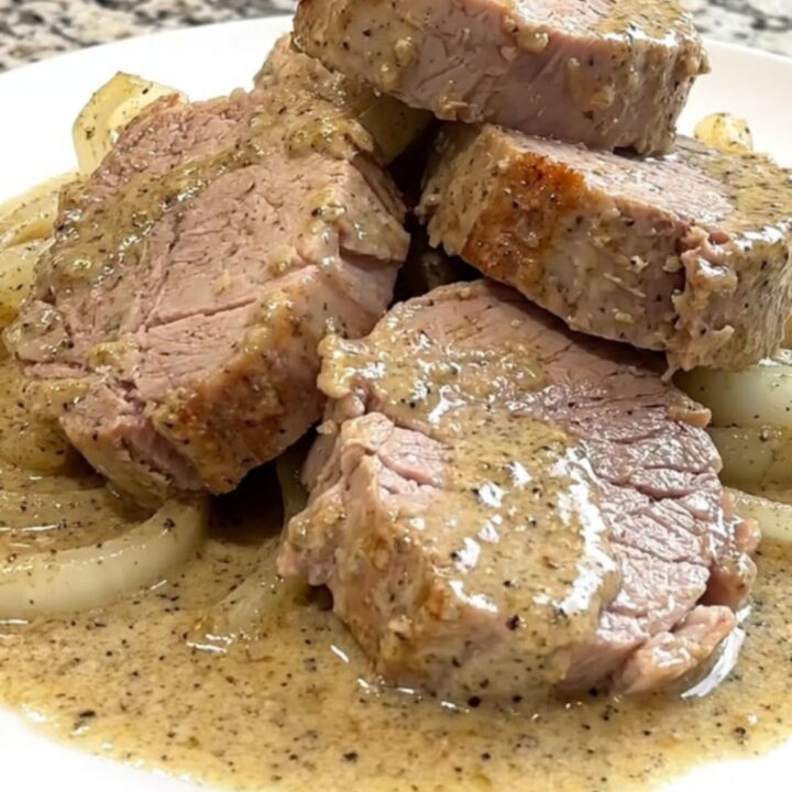 A close-up of tender pork medallions topped with a creamy peppercorn sauce and soft onions in a slow cooker.