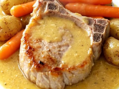 A top-down view of tender pork chops, carrots, and potatoes in a creamy honey Dijon sauce inside a slow cooker.