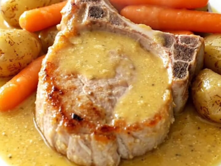 A top-down view of tender pork chops, carrots, and potatoes in a creamy honey Dijon sauce inside a slow cooker.