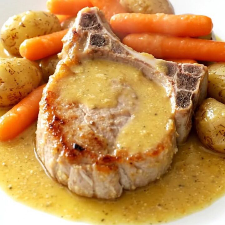 A top-down view of tender pork chops, carrots, and potatoes in a creamy honey Dijon sauce inside a slow cooker.