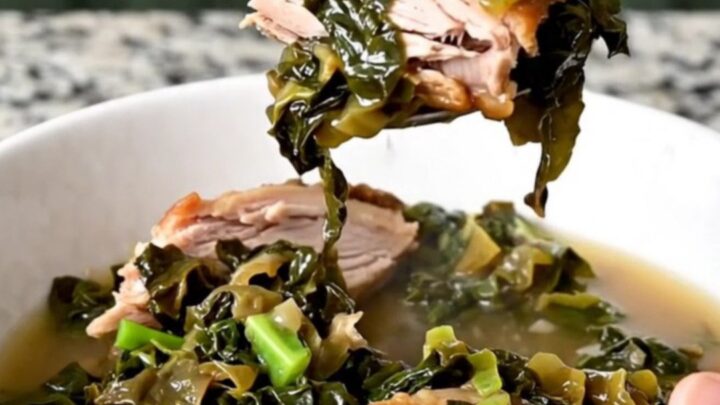 A white bowl filled with slow-cooked collard greens and pieces of smoked turkey in savory broth.