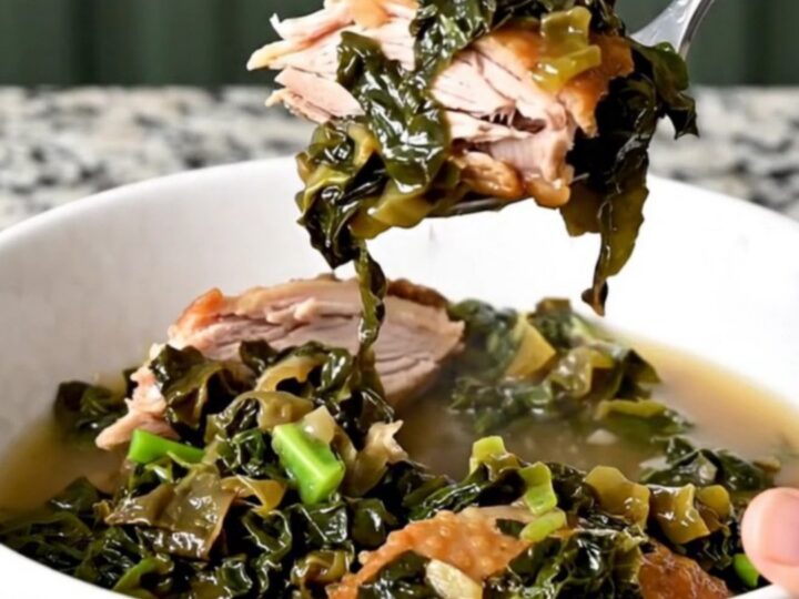 A white bowl filled with slow-cooked collard greens and pieces of smoked turkey in savory broth.