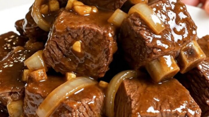 Slow cooker filled with tender beef cubes, onions, and a rich, glossy brown sugar garlic sauce.