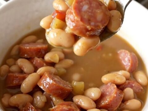 A warm, rustic bowl of creamy smoked sausage and butter bean stew garnished with fresh herbs.