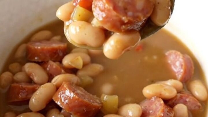 A warm, rustic bowl of creamy smoked sausage and butter bean stew garnished with fresh herbs.