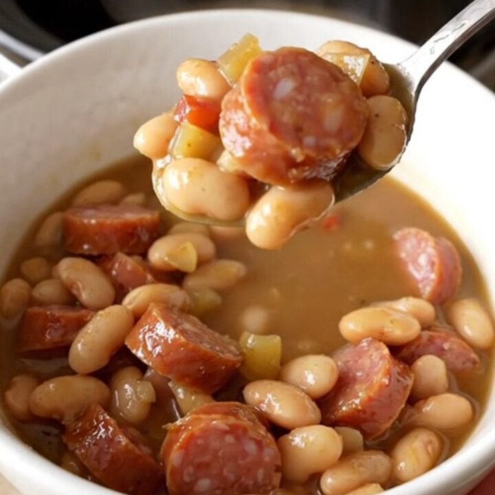 A warm, rustic bowl of creamy smoked sausage and butter bean stew garnished with fresh herbs.