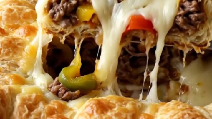 A golden, bubbling Philly cheesesteak crescent bake in a white ceramic dish on a wooden surface.