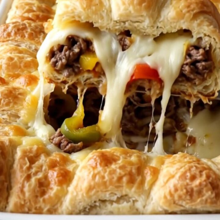 A golden, bubbling Philly cheesesteak crescent bake in a white ceramic dish on a wooden surface.