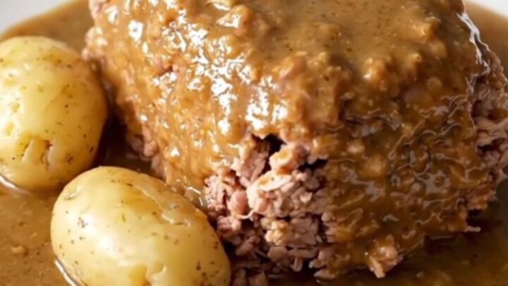 A close-up of a cooked turkey meatloaf in a slow cooker with baby potatoes and a creamy mushroom gravy.