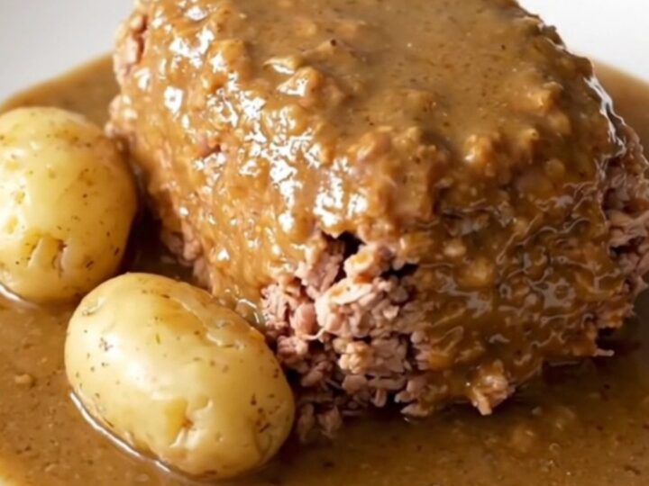 A close-up of a cooked turkey meatloaf in a slow cooker with baby potatoes and a creamy mushroom gravy.