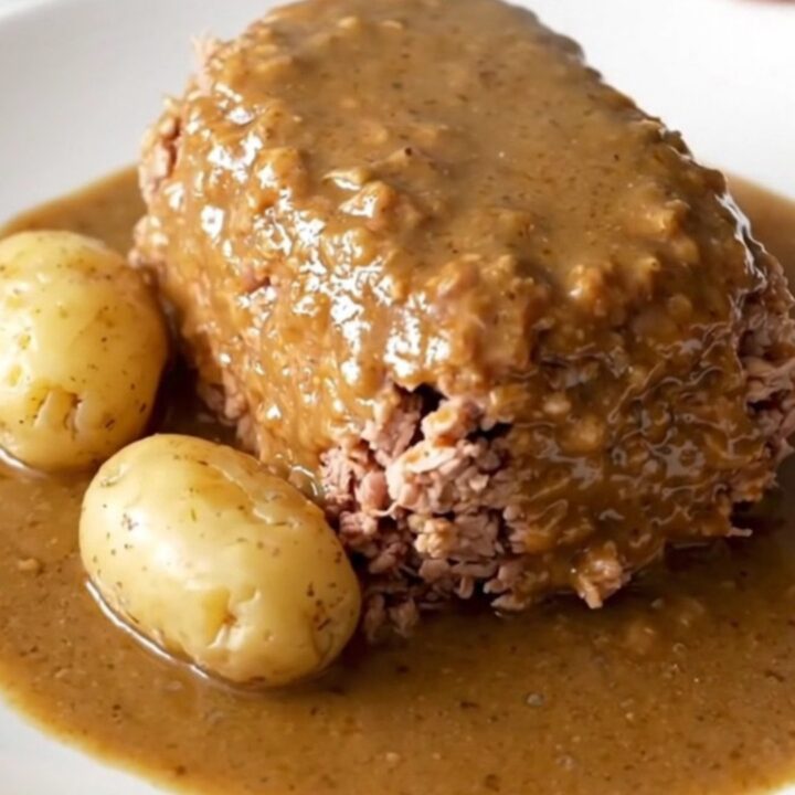A close-up of a cooked turkey meatloaf in a slow cooker with baby potatoes and a creamy mushroom gravy.