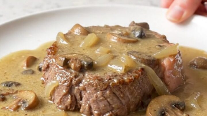 A close-up of tender cube steaks smothered in a thick, creamy mushroom and onion gravy served on a white plate.