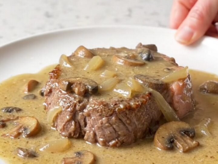 A close-up of tender cube steaks smothered in a thick, creamy mushroom and onion gravy served on a white plate.