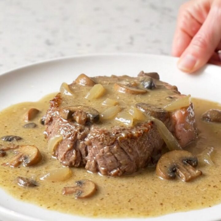 A close-up of tender cube steaks smothered in a thick, creamy mushroom and onion gravy served on a white plate.