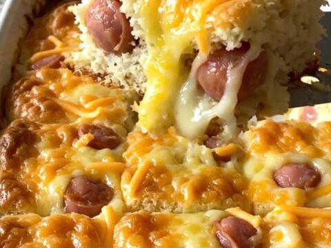 A top-down view of a rectangular baking dish filled with golden biscuits and mini sausages topped with melted cheddar.