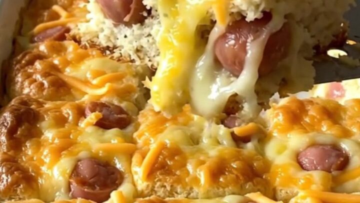 A top-down view of a rectangular baking dish filled with golden biscuits and mini sausages topped with melted cheddar.