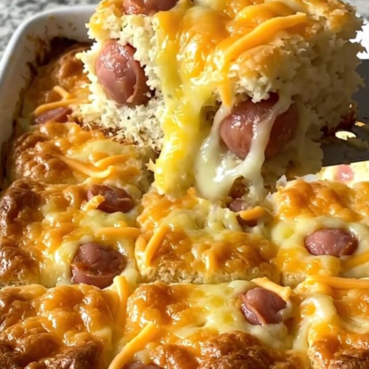 A top-down view of a rectangular baking dish filled with golden biscuits and mini sausages topped with melted cheddar.