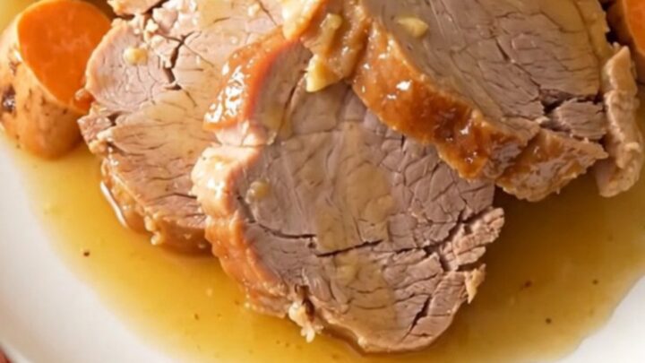 A slow cooker filled with a tender pork loin, sweet potato chunks, and onion wedges coated in a honey glaze.