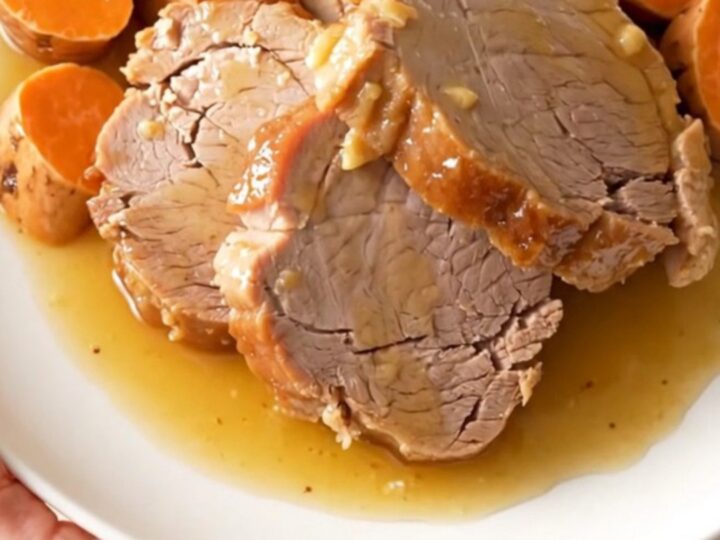 A slow cooker filled with a tender pork loin, sweet potato chunks, and onion wedges coated in a honey glaze.