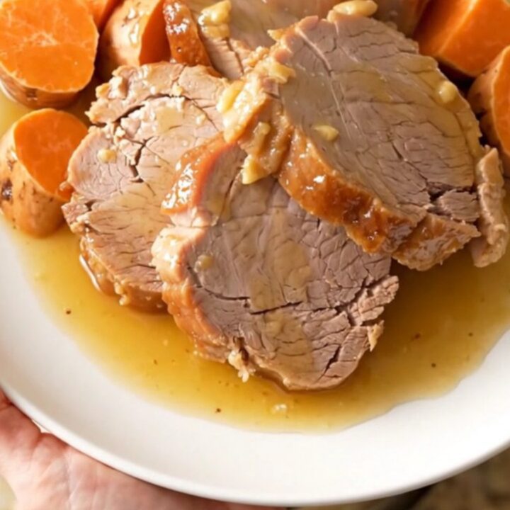 A slow cooker filled with a tender pork loin, sweet potato chunks, and onion wedges coated in a honey glaze.