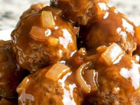 A slow cooker filled with glazed apricot barbecue turkey meatballs topped with diced onions and herbs.