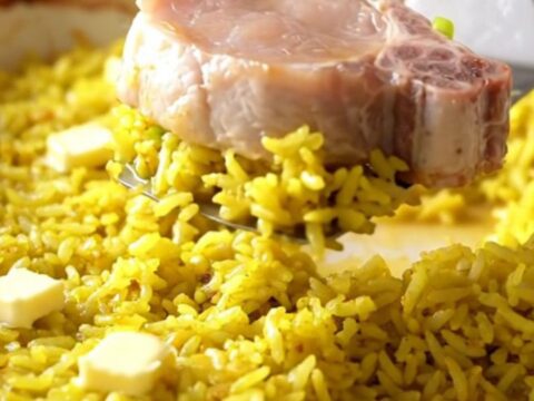 A top-down view of a rectangular baking dish filled with yellow rice and tender boneless pork chops.
