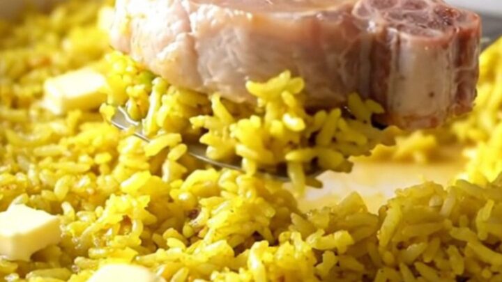 A top-down view of a rectangular baking dish filled with yellow rice and tender boneless pork chops.