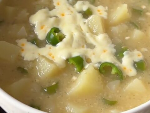 A warm bowl of creamy green chile potato soup with visible potato chunks and melted cheese.