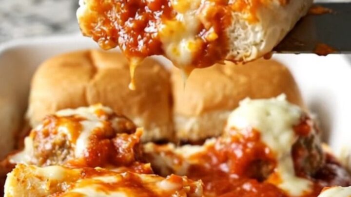 A close-up of golden-brown meatball sub sliders in a white ceramic baking dish.