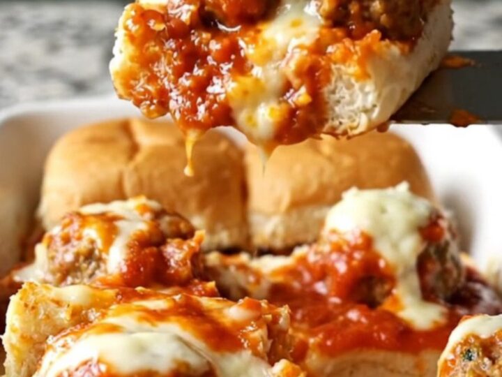 A close-up of golden-brown meatball sub sliders in a white ceramic baking dish.