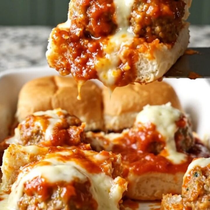 A close-up of golden-brown meatball sub sliders in a white ceramic baking dish.