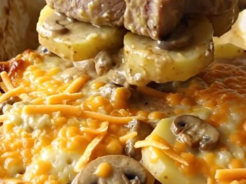 A ceramic baking dish filled with tender pork chops, sliced potatoes, and creamy mushroom sauce topped with melted cheddar.