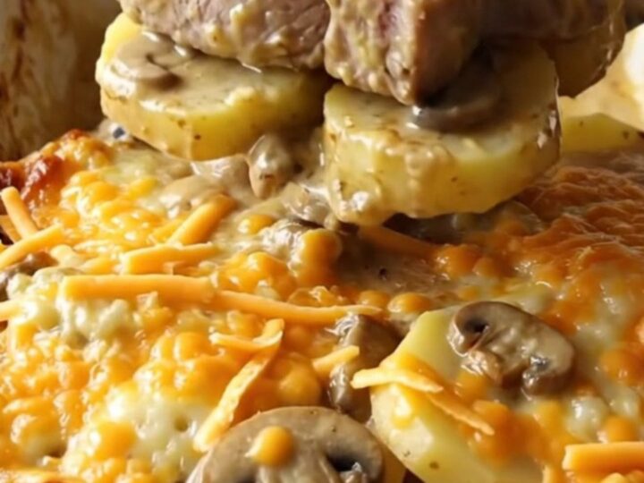 A ceramic baking dish filled with tender pork chops, sliced potatoes, and creamy mushroom sauce topped with melted cheddar.
