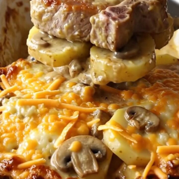 A ceramic baking dish filled with tender pork chops, sliced potatoes, and creamy mushroom sauce topped with melted cheddar.