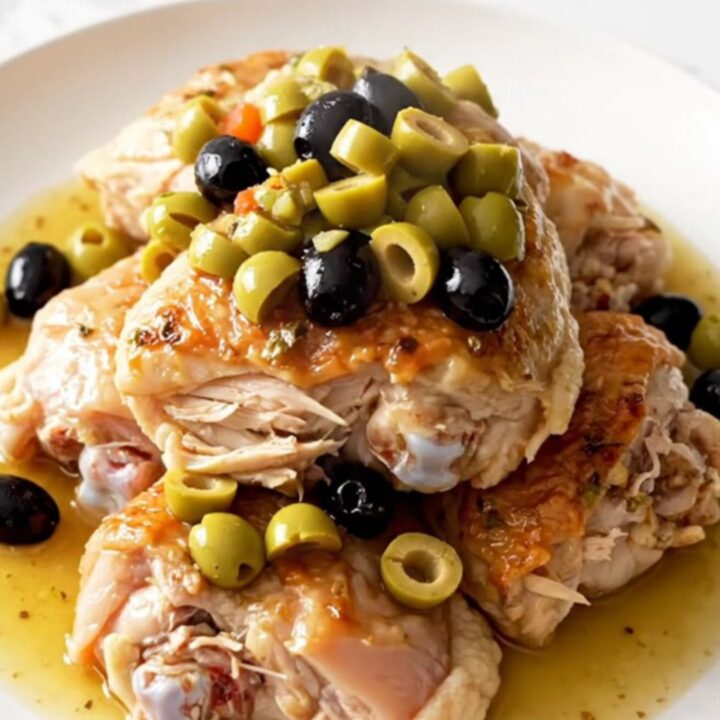A top-down view of slow cooker muffuletta chicken with visible pieces of olive salad and fresh herbs.