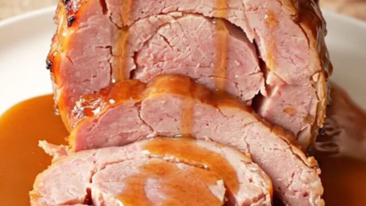 A close-up of a spiral-cut ham glazed with a glossy brown sugar and bourbon sauce in a slow cooker.