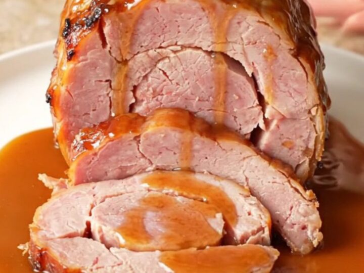 A close-up of a spiral-cut ham glazed with a glossy brown sugar and bourbon sauce in a slow cooker.