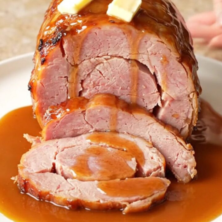 A close-up of a spiral-cut ham glazed with a glossy brown sugar and bourbon sauce in a slow cooker.