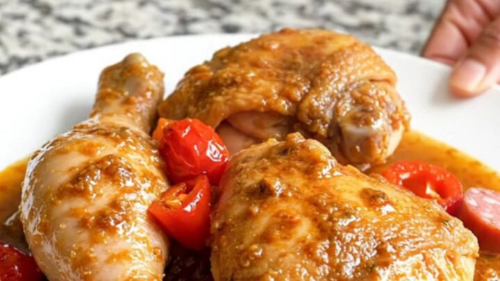 A top-down view of a slow cooker filled with chicken thighs, sliced sausage, and cherry peppers in a tangy sauce.