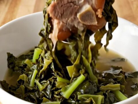A slow cooker filled with tender collard greens and savory ham hocks, ready to be served as a classic side dish.