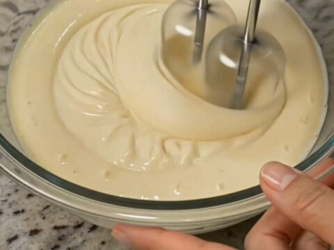 A clear glass bowl filled with a creamy fruit salad featuring sliced strawberries and grapes