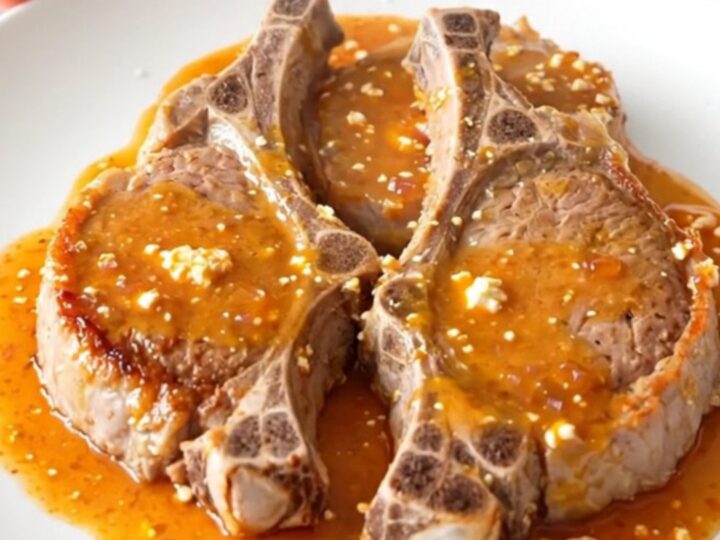 A top-down view of five raw pork chops in a slow cooker topped with red bell peppers and a block of cream cheese.