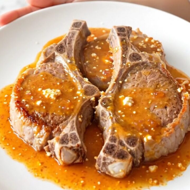 A top-down view of five raw pork chops in a slow cooker topped with red bell peppers and a block of cream cheese.
