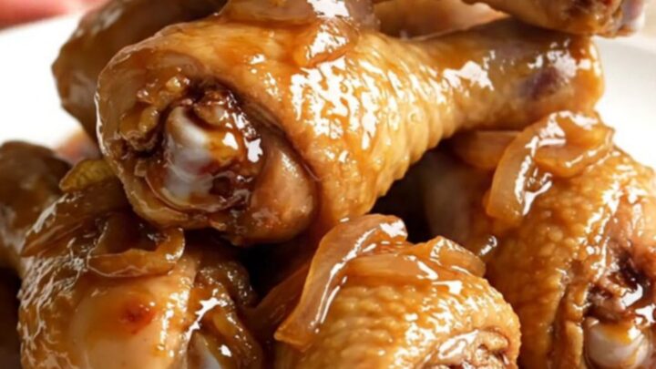 A high-angle shot showing raw chicken drumsticks arranged in a slow cooker with onions and sauce ingredients.