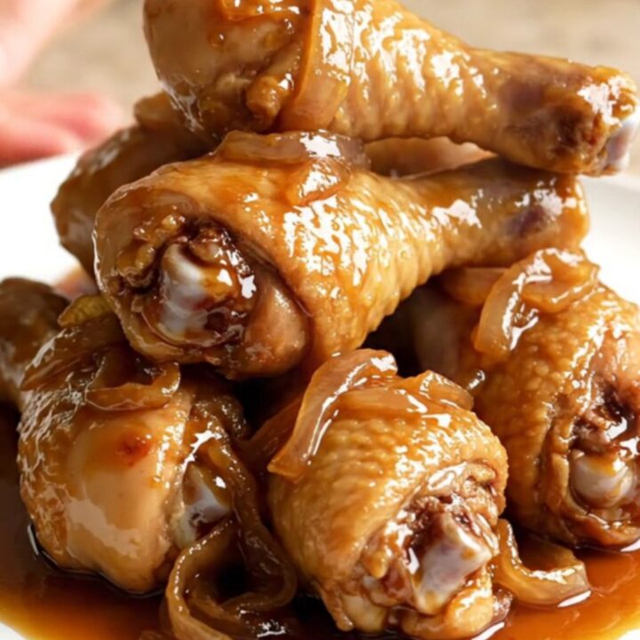 A high-angle shot showing raw chicken drumsticks arranged in a slow cooker with onions and sauce ingredients.