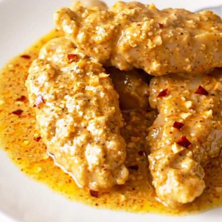A serving spoon lifting a tender piece of chicken coated in a rich