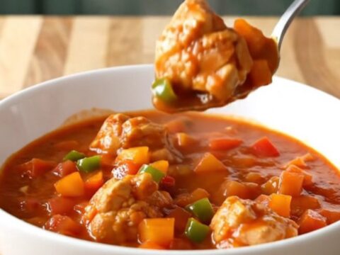 A close-up of chicken sauce piquante in a white bowl with steam rising, showing tender chicken and colorful peppers.