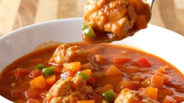A close-up of chicken sauce piquante in a white bowl with steam rising, showing tender chicken and colorful peppers.